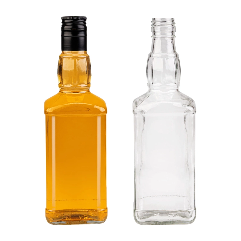 Dwie szklane flaszki Jack 500 ml, pusta i pełna bursztynowego bimbru, ze złotą zakrętką 28/38 obok siebie